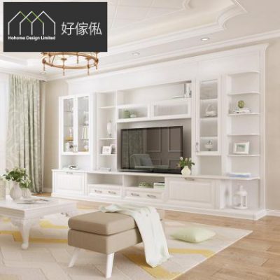 新古典客廳一角，雅緻白色電視櫃組合牆，中間電視位兩側為玻璃飾物櫃連開放層架擺放白瓶同相架，下方連抽屜地櫃；前方米色方形軟凳搭白色蓋毯，左方白色歐式茶几同淺綠窗簾，淺木地板鋪幾何花紋地氈。