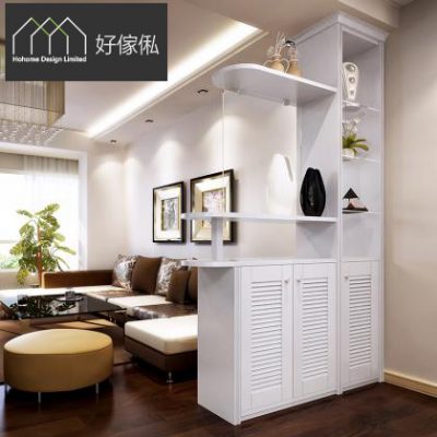 現代客廳實景，白色訂造玄關間隔櫃將玄關同梳化區分隔，右邊高身櫃連玻璃飾物層架擺擺設，白色弧形層板伸出，下層三道百葉趟門櫃，左邊牆掛兩幅黑框畫，前方有啡色梳化、深木茶几同圓形腳踏。