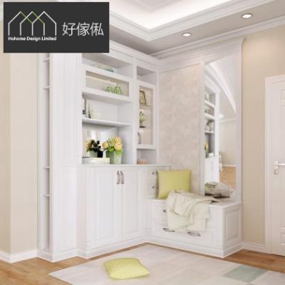 雅緻白色轉角玄關櫃近景，左方連門鞋櫃連上方開放層架擺放鮮花同擺設，右方轉角設換鞋長凳鋪坐墊放嫩綠色抱枕同淺色衣物，旁邊接拱形門口；淺木地板鋪黃綠色方形地墊放抱枕。
