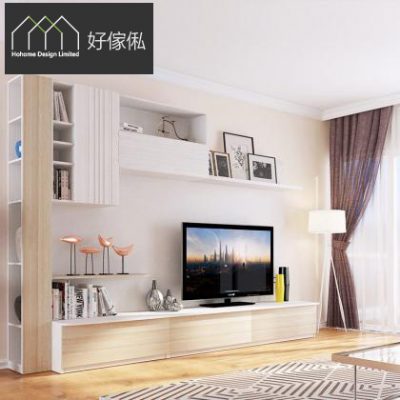 客廳電視牆場景，牆身做暖白色配淺木紋訂造組合，左邊一支高身開放式層架擺擺設，中間牆上裝飄櫃同白色層板放相架，下方一條長身電視地櫃放平面電視同檯燈，旁邊一支座地燈，右邊落地窗配啡色窗簾，地面鋪幾何圖案地氈同淺色木地板。