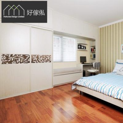 睡房實景圖，左上角好傢俬 HoHome 標誌，左邊頂天立地淺木紋趟門衣櫃中央嵌啡色花葉雕花面板連頂櫃，中間靠窗書枱配層板書架同窗台坐墊，右邊淺木雙人床鋪藍綠波浪床品，地面鋪深啡實木地板。