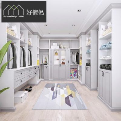 北歐風衣帽間，兩側灰白開放掛衣櫃連抽屜層架，掛滿外套同摺疊衣物，中央玻璃門飾櫃放手袋擺設，地面鋪灰黃幾何圖案地毯，左邊大型綠葉植物，淺木地板，整體灰白色調明亮通透。