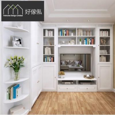 純白色電視組合櫃，中央凹位嵌入平面電視，上方同兩側開放層格擺滿書本同飾品，電視下設白色台面連兩個抽屜，左邊轉角圓弧層架放百合花同書本，配淺色木地板。