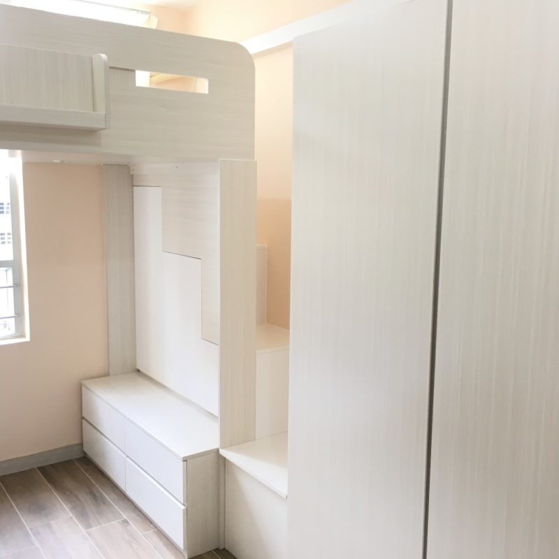 公屋單位訂造嘅整套淺木紋傢俬全景，左邊係上格組合床連圓邊開窗床頭板，中間白色階梯式樓梯櫃連抽屜踏級上落，右邊係一幅頂天直紋掩門大衣櫃，地面鋪深啡色木紋地磚。