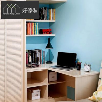 訂造轉角電腦枱近景，左上好傢俬商標，淺木色L形枱面擺住打開嘅手提電腦、黑色檯燈、筆筒同鬧鐘，上方藍牆設多層開放書架擺滿書本擺設，枱下開放收納格放白色收納箱，左邊見白色百葉衣櫃門。