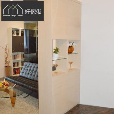 玄關間牆櫃側面實景，淺木紋色高身雙面櫃做間隔牆，中段鏡面中空格設玻璃層架，放有白花、綠色盆栽、棕色花瓶同金屬高腳杯，左方係黑色皮梳化、書架同玻璃茶几嘅客廳，鋪淺色地氈同深色木地板，左上角有好傢俬 HoHome 標誌。