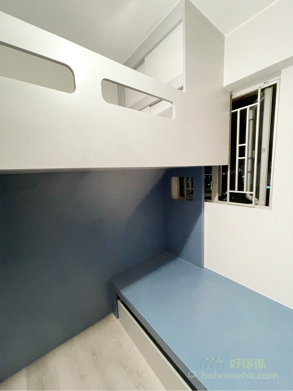 訂造組合床下層，藍灰色平台床貼住窗邊延伸，床身下方設一個淺灰色大抽屜，後方深藍色牆身，右側白牆連開揚式鋁窗，地面淺色木紋地板。