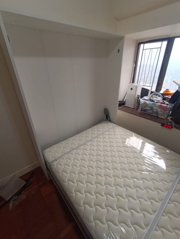 窗邊房間內的白色Livo 5尺直翻變形床已向下打開，白色花紋雙人床褥平放於床架，床箱內側及灰色支撐臂清楚可見。