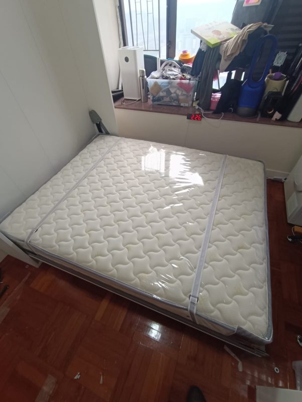 香港家居房間內的白色Livo 5尺直翻變形床已打開，白色花紋床褥放在金屬床架上，旁邊是木地板及窗台。