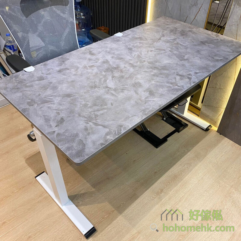 Morton電動升降枱佩茲利限定色俯視實拍，枱面呈深灰色大理石裂紋質感，四角設有白色保護角，升降金屬腳可見於枱面下方，背景為木地板及白色展示場地。