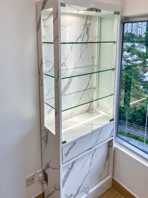 窗旁窄身展示櫃設透明層板，背板及下方櫃門呈白色石紋