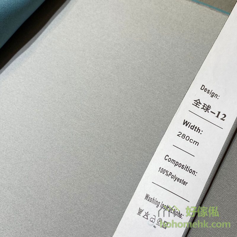 斜紋平板布窗簾12號色布料近距特寫，標籤顯示「全球-12」及100%Polyester，布面呈細密斜紋素色設計