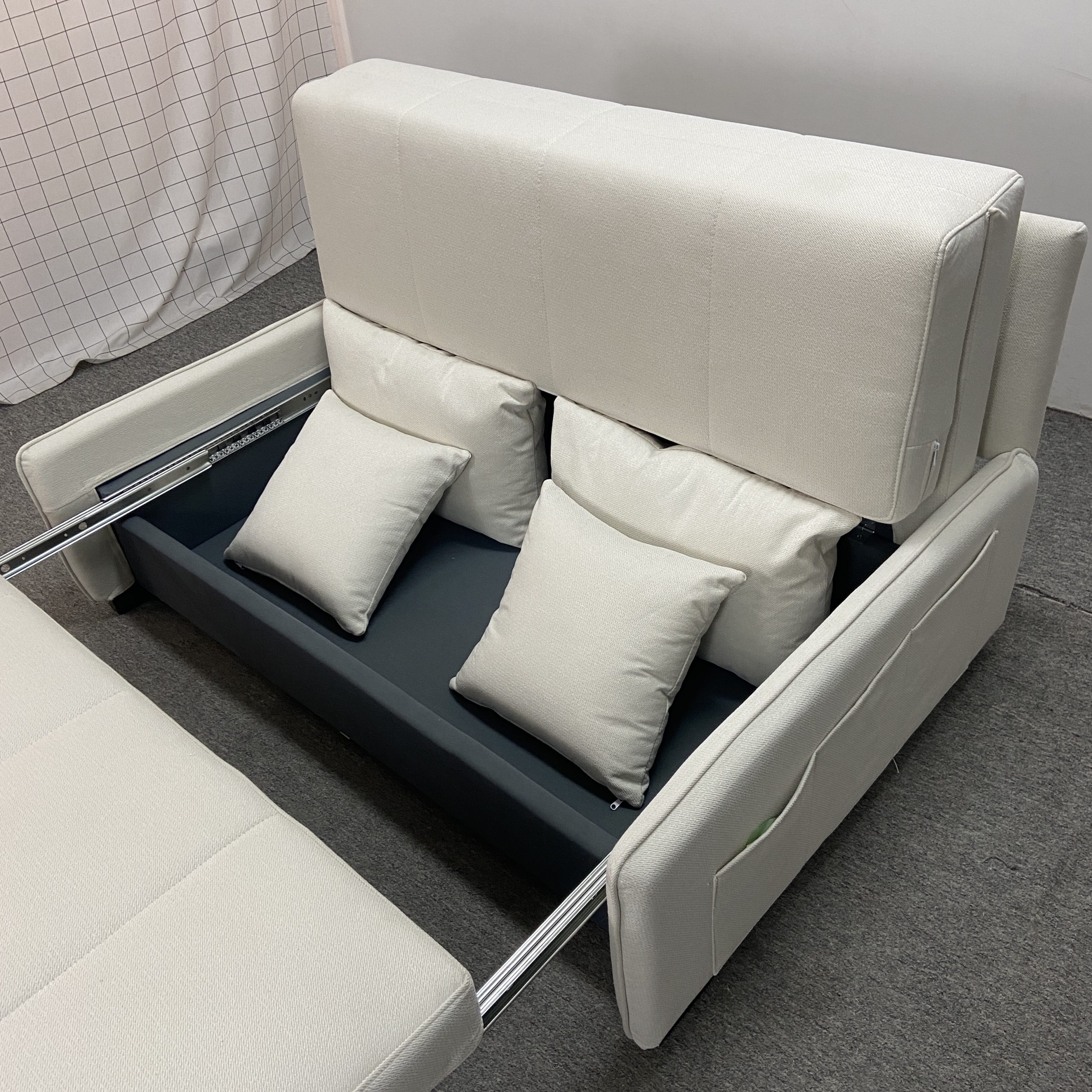 Takumi 6079款矮扶手版本米白色布藝梳化床拉開後底部儲物格近距離照，可見黑色儲物盤、銀色不銹鋼滑軌，背靠分開升起，白色牆面背景