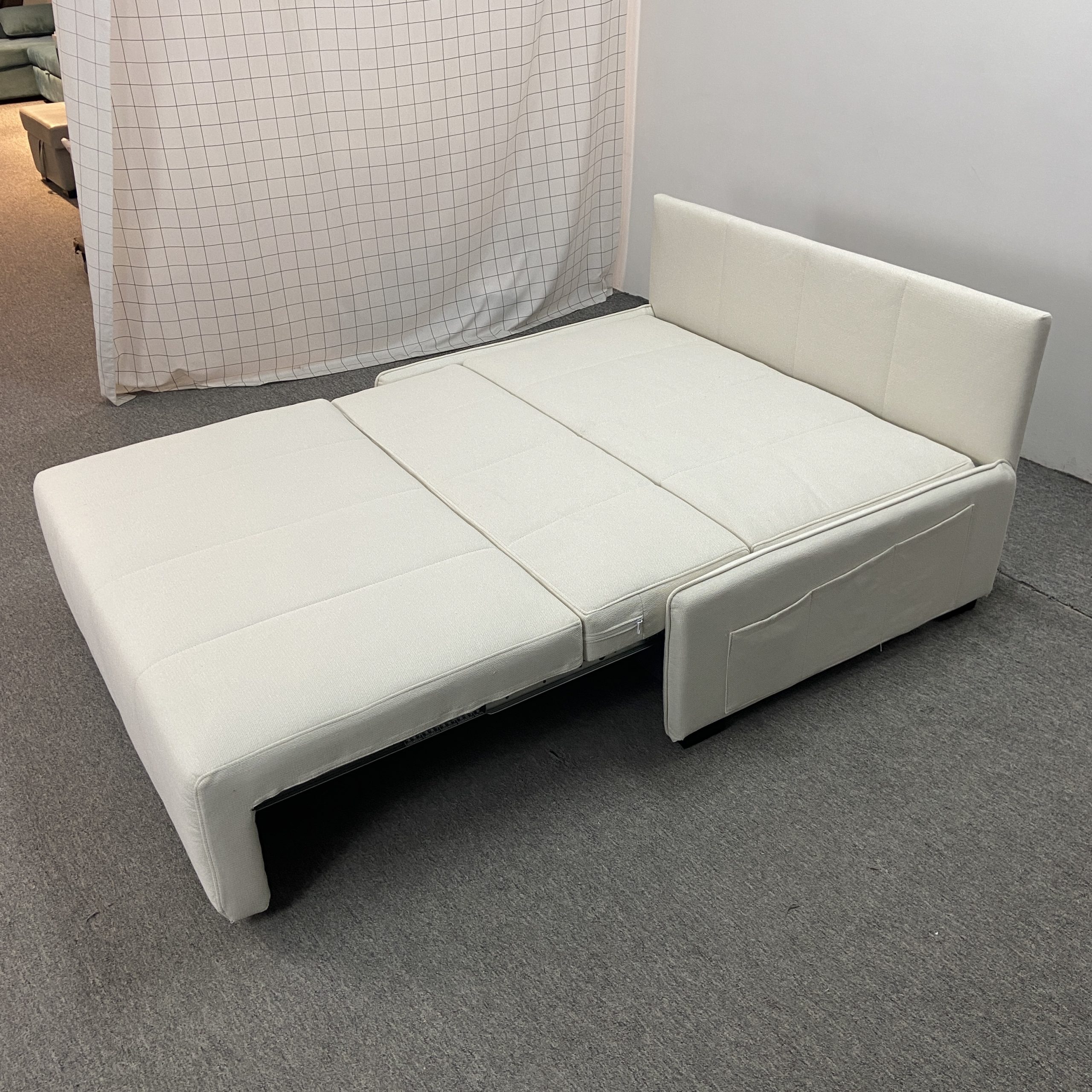 Takumi 6079款矮扶手版本米白色布藝梳化床展開為床的前側面照，銀色不銹鋼導軌可見，床面鋪設平整，配米白抱枕，工廠背景拍攝