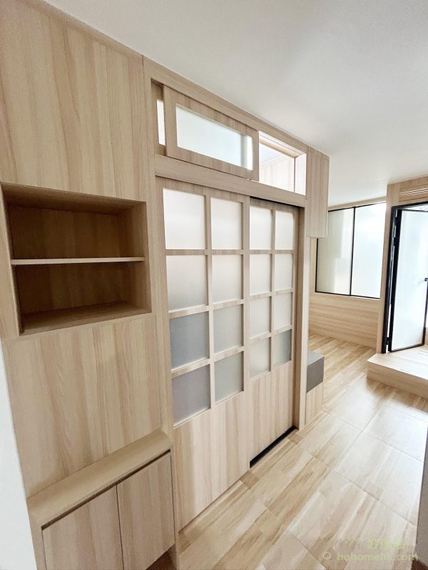 香港公屋訂造間房實景：入口處淺木色夾板間房牆，左側設開放式書架層板及有門儲物底櫃，中間為日式格子磨砂玻璃趟門，上方橫窗讓光線穿透，右側可見另一間磨砂玻璃房門，地板鋪淺色木紋地板。