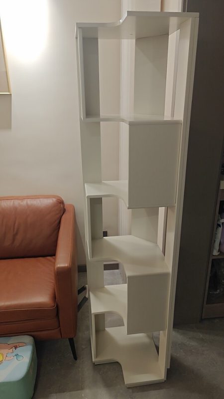 客人白色款Peyton落地儲物書架實拍，擺喺客廳角落靠牆位置，左邊係磚紅色皮革梳化配黑色金屬腳，牆身白色，書架空層冇擺嘢方便睇清階梯式結構同白色烤漆表面