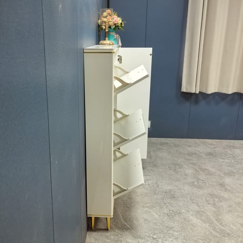 深藍色牆前，奶油白色亮光面鞋櫃側面拍攝，可見到 3 個翻斗式門全部向外傾斜打開，櫃頂放金色玻璃燭台同青色花瓶插繡球花，右邊有米色窗簾，灰雲石地台。