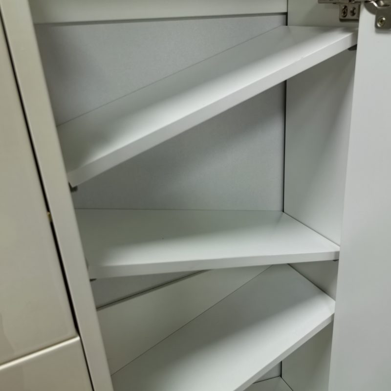 白色亮光面鞋櫃內部近攝，可見 4 至 5 層向外傾斜嘅白色收納板結構，右邊為打開中嘅直紋櫃門連銀色鉸鏈，左邊為櫃門內側，燈光柔和照落斜板面。
