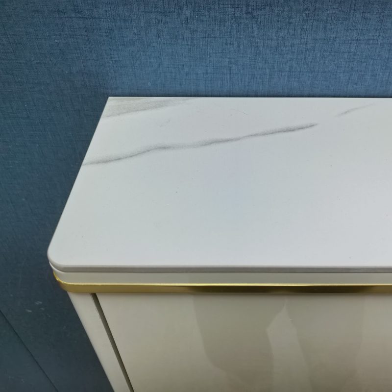深藍色布紋牆前近攝，奶油白色亮光面鞋櫃頂部特寫，枱面採用白色雲石紋岩板，枱面同櫃身之間有一條金色金屬收邊，亮光焗漆櫃身可見反射光暈。
