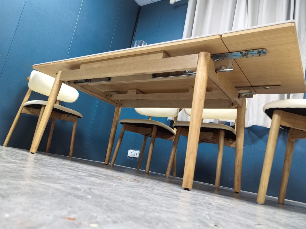 由地面向上拍攝Reese伸縮餐枱底部，原木色實木橫樑、中央承托架、金屬滑軌及延伸板五金連接件清楚外露，四支木枱腳分置角位。
