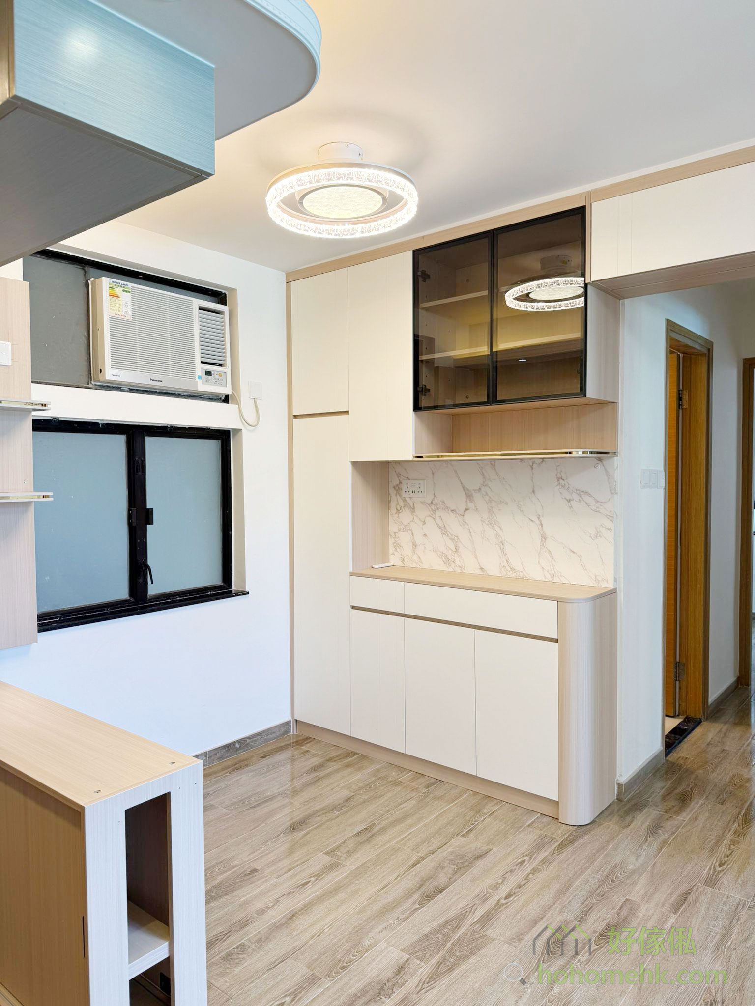 廚櫃、浴室櫃及客廳、睡房的訂造傢俬均採用相同的材質及設計風格，令整個單位的視覺效果顯得更為統一。無論是廚房的潔白牆身，還是浴室的簡約線條，每一件訂造傢俬都體現了細緻的工藝。開放式廚房選擇灰杏色和大面積的奶油色，使整個客廳空間顯得更寬敞光亮。