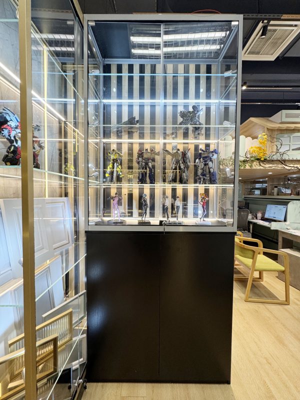 黑色幼框玻璃展示櫃正面全景，透明櫃門內設多層玻璃層板、白色燈帶及黑金間條背板，上層陳列機械人模型，下層排列多款人偶，底部為黑色雙門櫃。