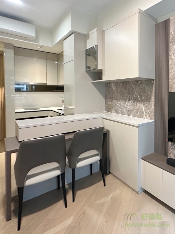 廳櫃與吧枱的設計不僅是廚房與客廳的分隔，更能透過石面枱面的延伸大幅增加廚櫃的工作枱面。特別是錯層的創新設計，讓餐枱藏於吧枱之下，需要時可拉出變成獨立餐枱，節省空間之餘，亦讓中島更具層次感與特色，滿足現代家庭對靈活性的需求。