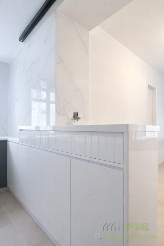 廚房採用半開放式設計，以吧枱作為廚房與客廳的分隔。吧枱由廚櫃延伸而成，不僅增加了工作枱面的面積，還提升了空間的互動性。無論是煮大餐還是招呼朋友，這樣的設計都讓生活更加方便、愜意。