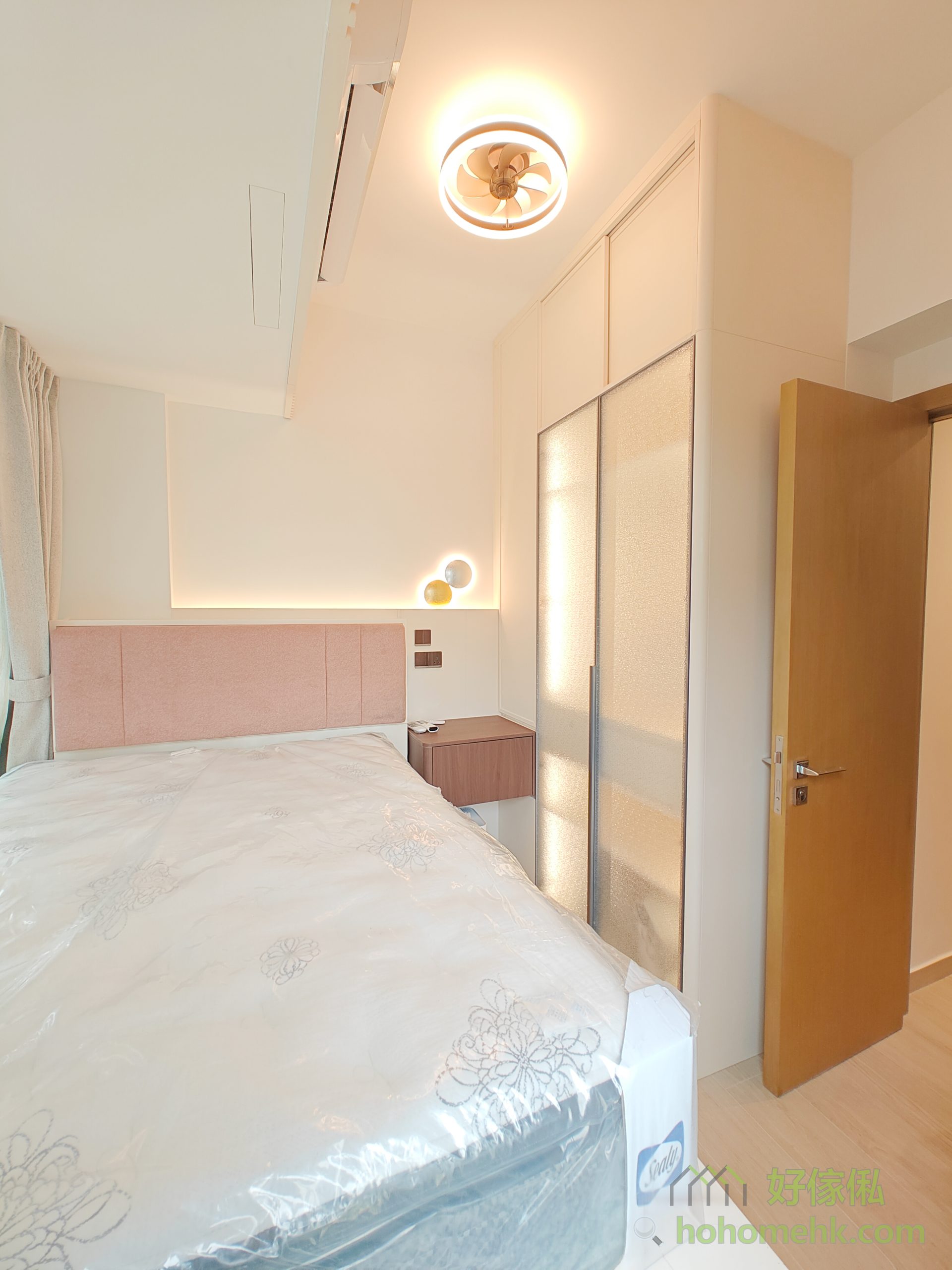 床頭以粉色布藝cushion作設計亮點，營造出舒適柔和的空間氛圍，非常適合休息及放鬆心情。這款布藝選材不僅能滿足業主對溫馨氛圍的期待，亦在耐用性和美觀性上達至完美平衡。床頭牆上的壁燈進一步豐富了光影效果，讓房間顯得更加精緻且富有層次感。