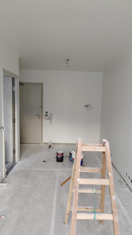 屯門業旺邨客廳油漆施工現場，白色牆身及天花完成批灰髹漆，灰色地面鋪上保護物料，前方有木梯、油漆桶及施工工具。