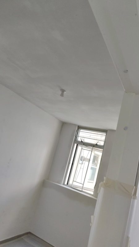 細睡房以白色牆身配灰白色批灰天花，畫面右側有牆柱及開關位，盡頭設鋁框窗連鐵花，地腳線沿牆角鋪設，現場仍在髹油前基層處理階段。